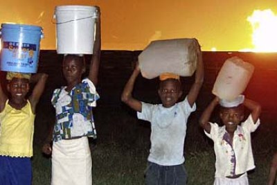Nigerian children collect water close to gas flares: The country generates U.S. $100 million a day from oil, but fewer than half the people have running water.