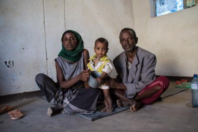 A family sits on the floor of their home with their one-year-old son, who has moderate acute malnutrition.