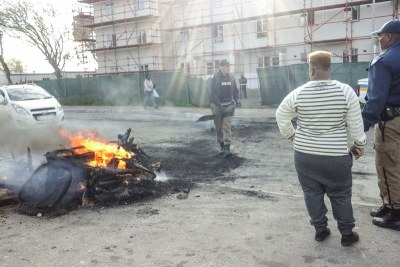 A police officer attempts to extinguish a fire during a service delivery protest in Langa, Cape Town.