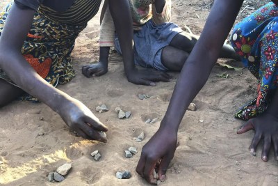 Trois jeunes filles jouent avec des cailloux en guise de pions (jeu « isolo ») sur un terrain sableux dans la commune de Waya à Kabwe, en Zambie. Or, elles s’exposent ainsi à des poussières de plomb toxique, dont les taux sont particulièrement élevés dans les sols de cette zone.